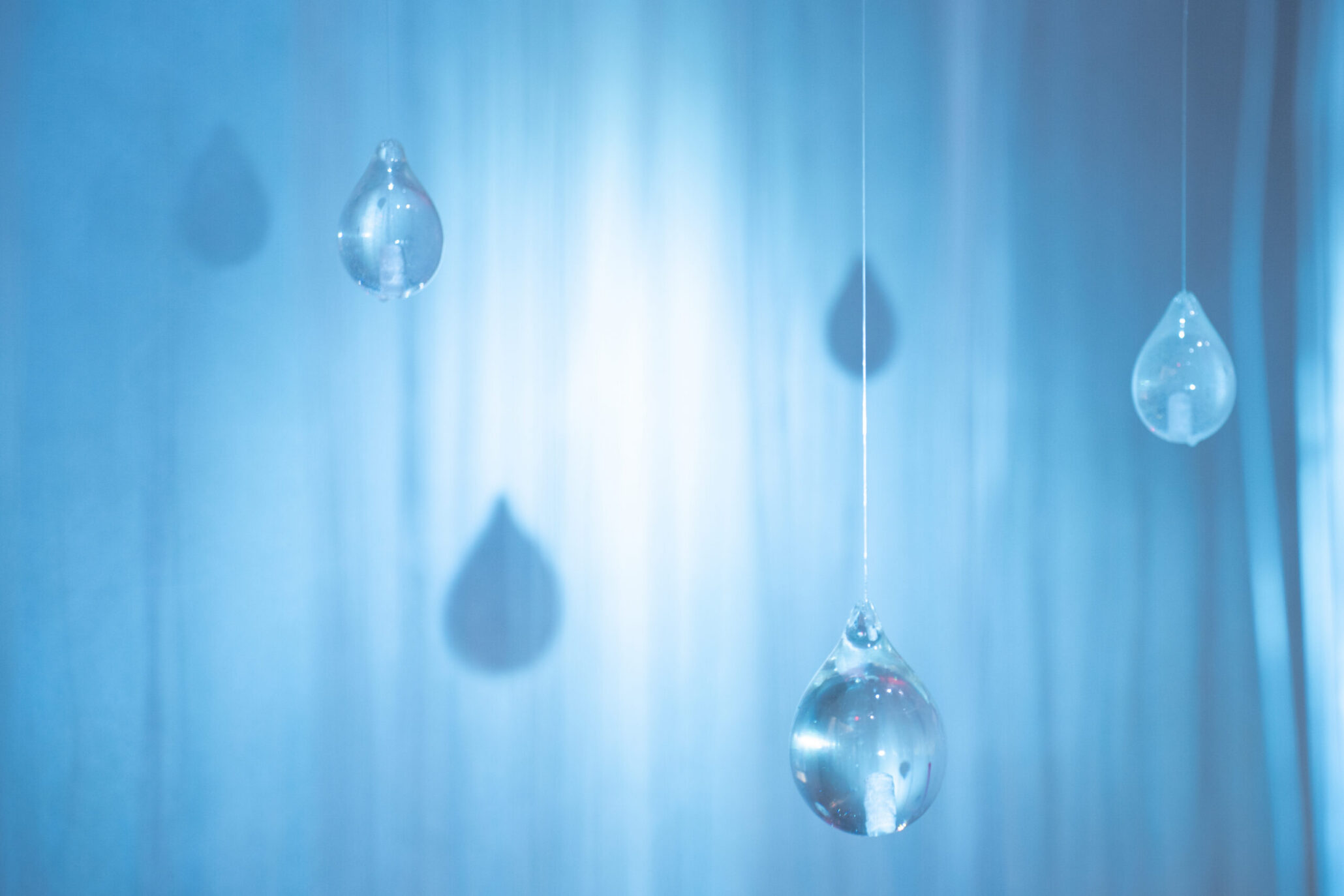 Blue background with several hanging glass droplets reflecting light on strings or cords.